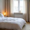 Et mykt beige teppe under en seng i et soverom med maritim innredning og havutsikt.